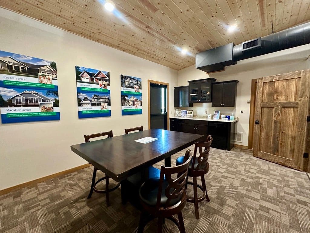 Modern interior of a meeting room with a wooden table, kitchen area, and display boards.